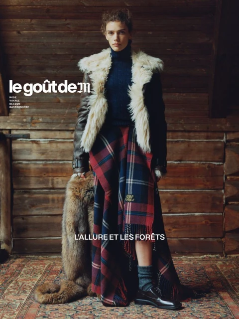 Fashion editorial shot of a woman in a fur-trimmed jacket and plaid kilt standing in a wood-paneled room, holding an animal pelt.