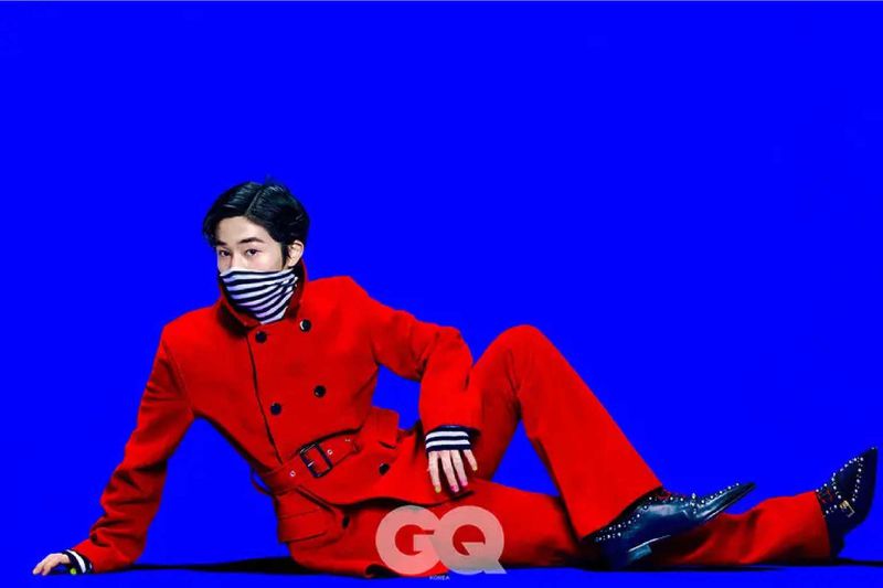 A striking portrait of a person in a red suit and black shoes against a bright blue background, conveying style and confidence.
