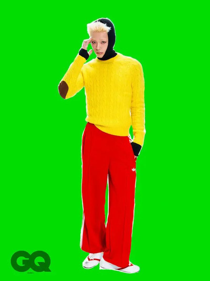 Fashion editorial shot of a man in a yellow sweater, red pants and black hood against a green background with 'GQ' logo visible.