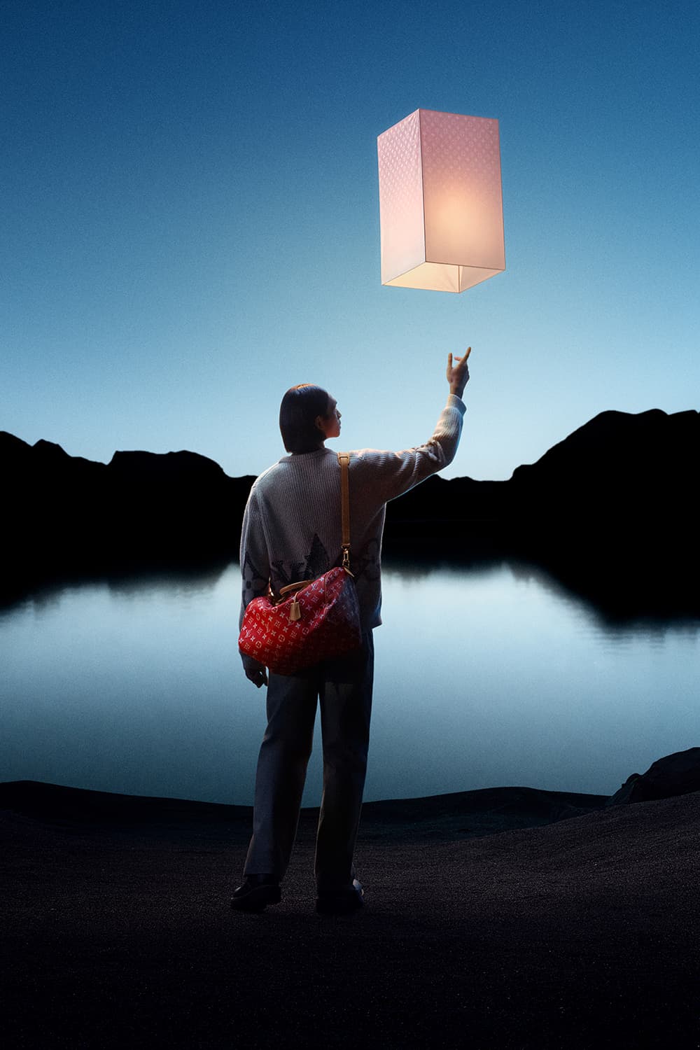 Adult reaches for glowing lantern in a serene nighttime landscape with a dark lake and mountain silhouettes under a clear twilight sky.