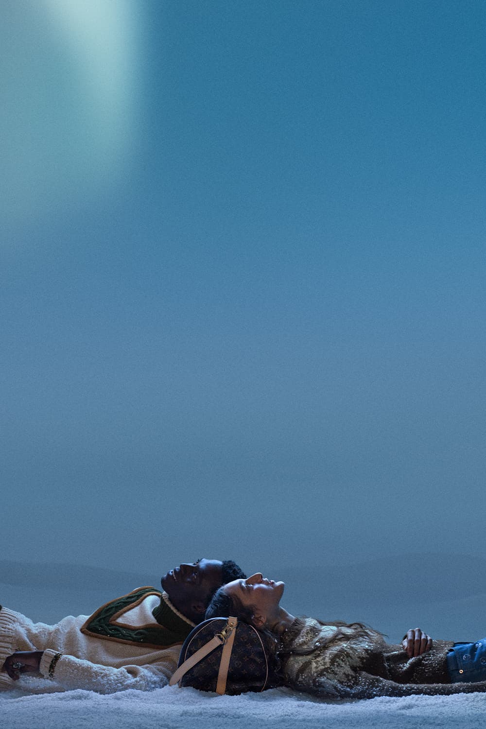 Two people lying in the snow beneath a cool blue sky for Louis Vuitton Holiday 2025 campaign