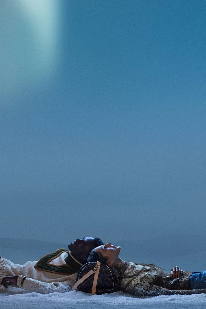 Two people lying in the snow beneath a cool blue sky for Louis Vuitton Holiday 2025 campaign
