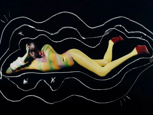 A dark-skinned woman in patterned bodysuit lies against a black background with white line art, wearing large red earrings and red shoes.