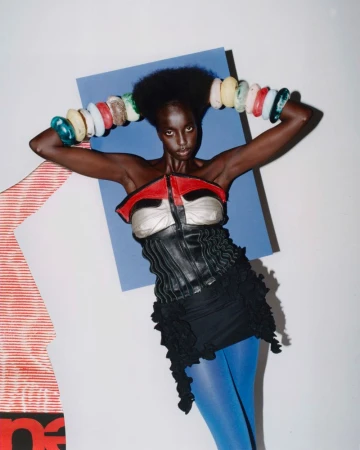 Woman in avant-garde fashion poses in front of blue and white geometric background with large, colorful bangle bracelets and blue tights.