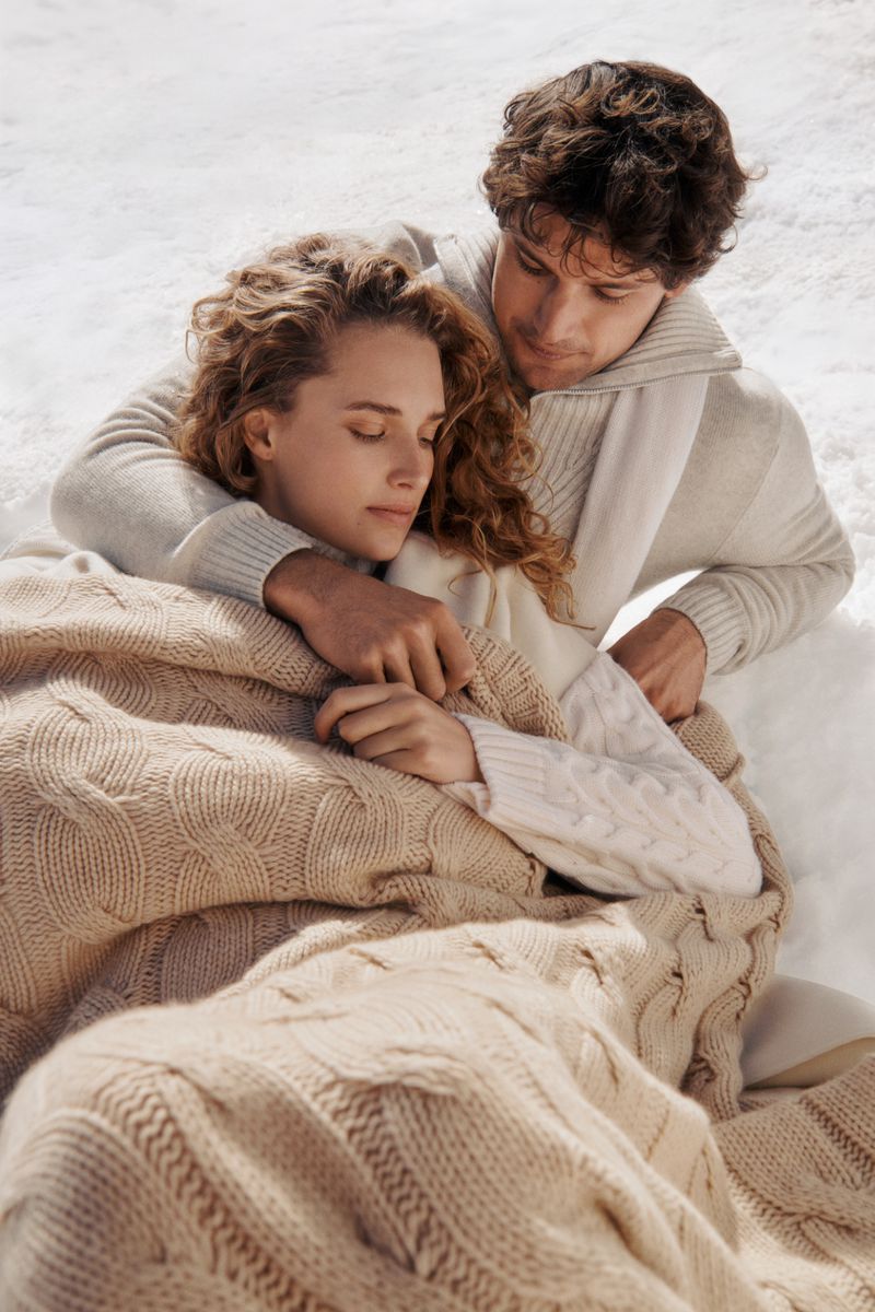 Romantic image of a couple embracing outside in winter. The woman is wrapped in a knitted blanket, with light and airy feel.
