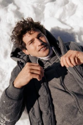 Model Giacomo Cavalli lying in snow wearing a grey knit zip-up jacket for the Falconeri fall winter 25 campaign