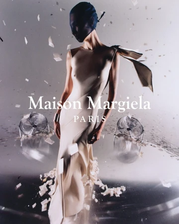 Fashion editorial shot of a woman in a light-beige gown with a dark-blue sheer veil, posing on a reflective surface with confetti.