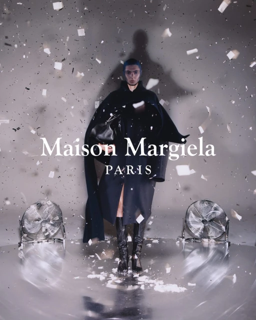 A fashion shot of a person in dark clothing standing amid confetti on a reflective floor, flanked by two fans, and logo text overlay.