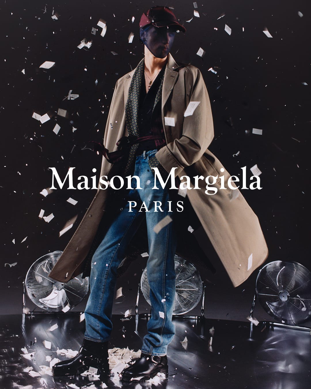Fashion shot: Person wearing a beige trench coat, blue jeans, and black boots, with scattered white confetti on a dark background.
