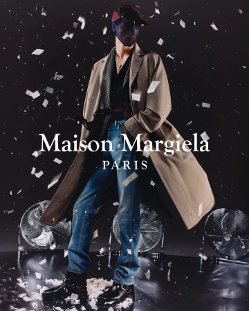 Fashion shot: Person wearing a beige trench coat, blue jeans, and black boots, with scattered white confetti on a dark background.