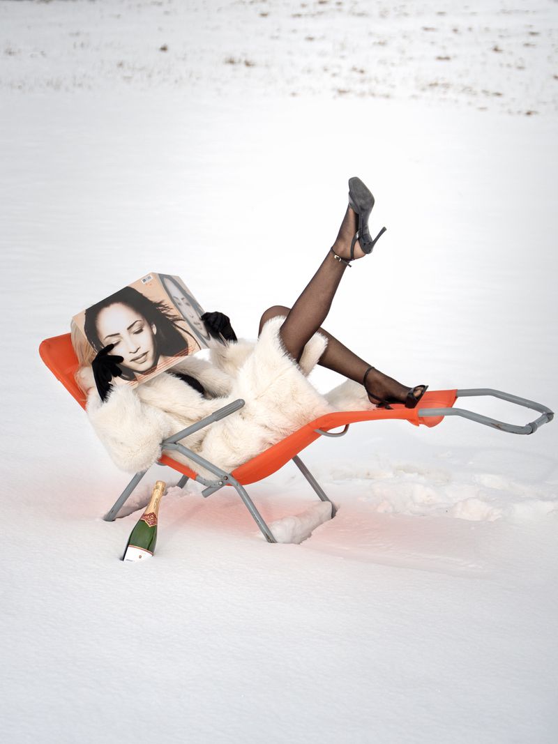 Woman in fur coat and heels lounges in a beach chair in the snow with champagne and a magazine. Outdoor fashion and lifestyle shoot.
