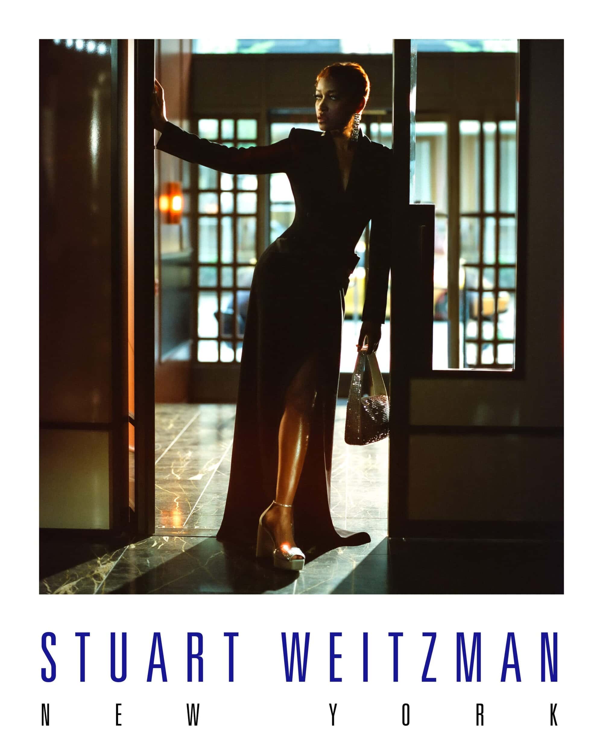 A stylish woman in a black dress and metallic heels poses in a doorway for a Stuart Weitzman New York fashion campaign.