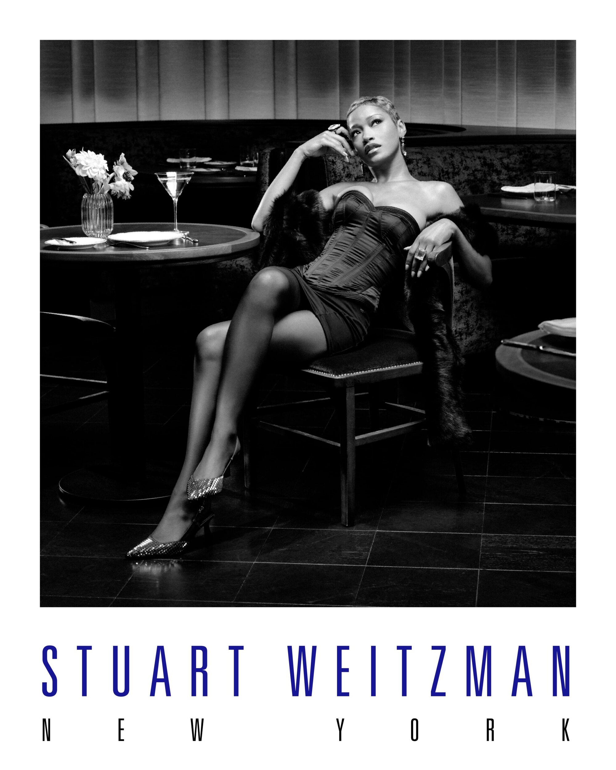 A stylish black and white fashion shot featuring a woman in an elegant dress and sparkling shoes, posing in a sophisticated bar setting.