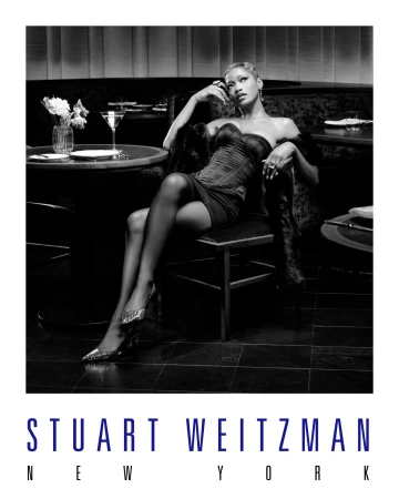 A stylish black and white fashion shot featuring a woman in an elegant dress and sparkling shoes, posing in a sophisticated bar setting.