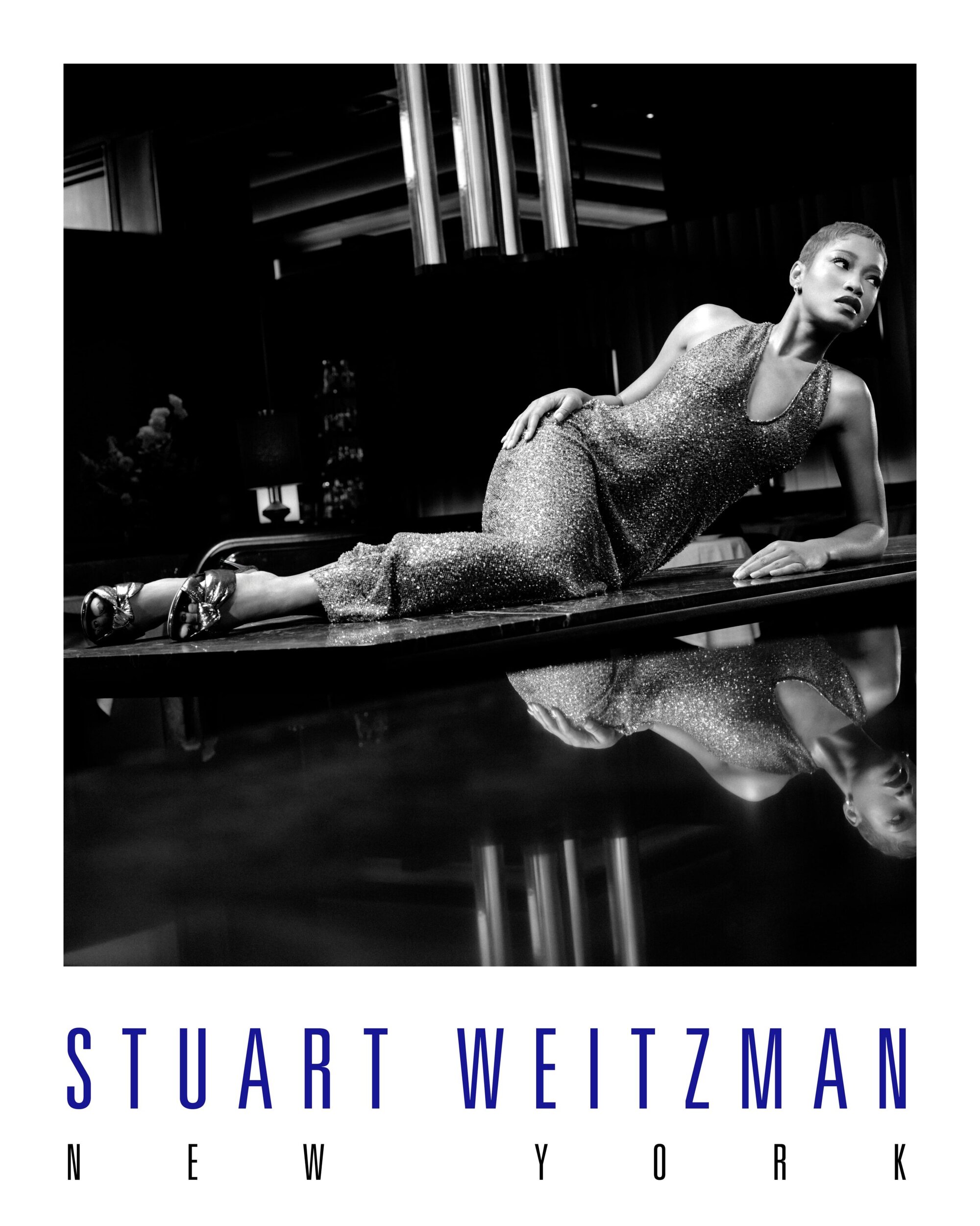 Keke Palmer reclining on a reflective surface wearing a sequined dress for Stuart Weitzman Holiday 2025 campaign.