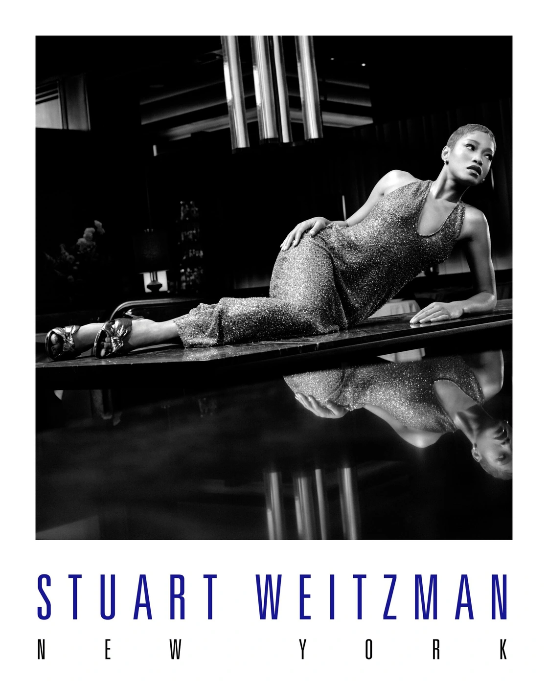 Keke Palmer reclining on a reflective surface wearing a sequined dress for Stuart Weitzman Holiday 2025 campaign.