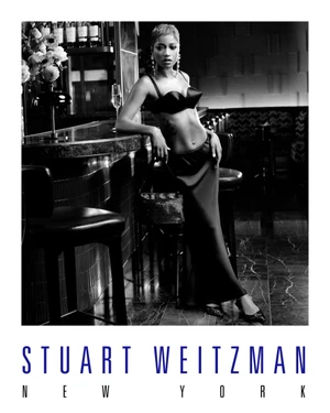 Keke Palmer leaning against a bar in a black outfit for Stuart Weitzman Holiday 2025 ad campaign, photographed in black and white.
