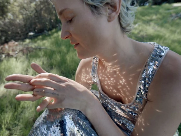 Close-up portrait of actress Vicky Krieps wearing a silver sequined dress outdoors with dappled sunlight on her skin
