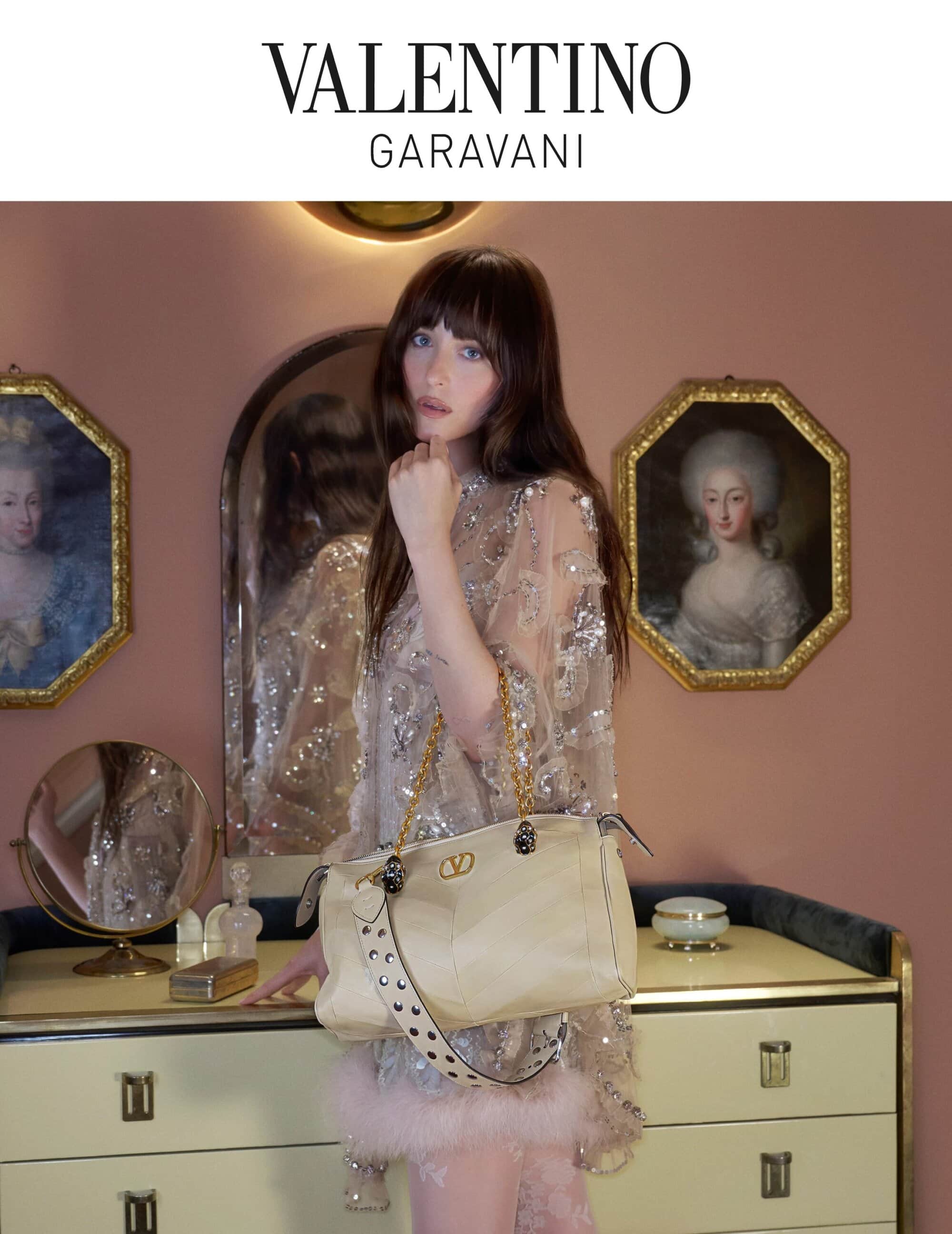 Elegant woman with Valentino Garavani bag in a chic setting with paintings and a vanity, showcasing luxury and classic style.