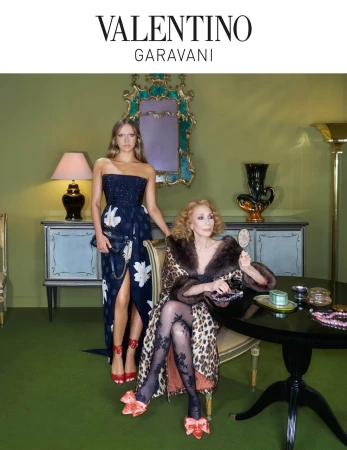 Two women pose in an opulent setting; one seated in a leopard coat, the other standing in a formal gown, showcasing Valentino Garavani.