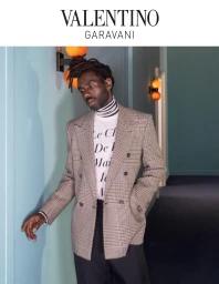 Man wearing a plaid double-breasted blazer and striped turtleneck in a corridor for Valentino