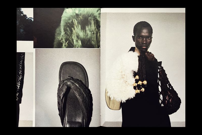 Editorial fashion shot of an African woman in a black outfit wearing a white fluffy shawl with a necklace and carrying a handbag.