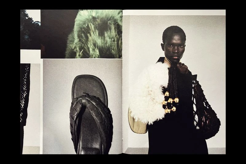 Editorial fashion shot of an African woman in a black outfit wearing a white fluffy shawl with a necklace and carrying a handbag.