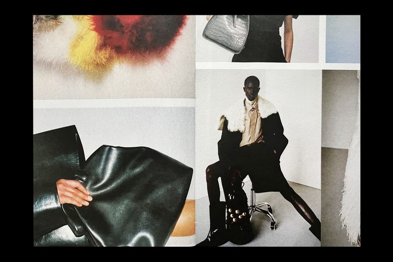 Two-page magazine spread. One male model poses on a silver office chair in a black coat; a hand grips a shiny black bag on the left.