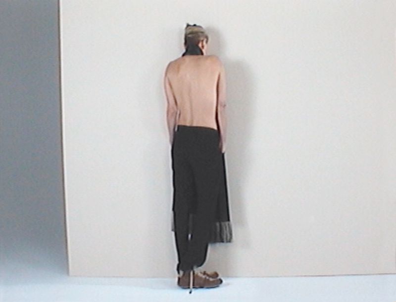 Charlize Theron shown from behind wearing dark trousers against a pale studio background for AnOther Magazine.