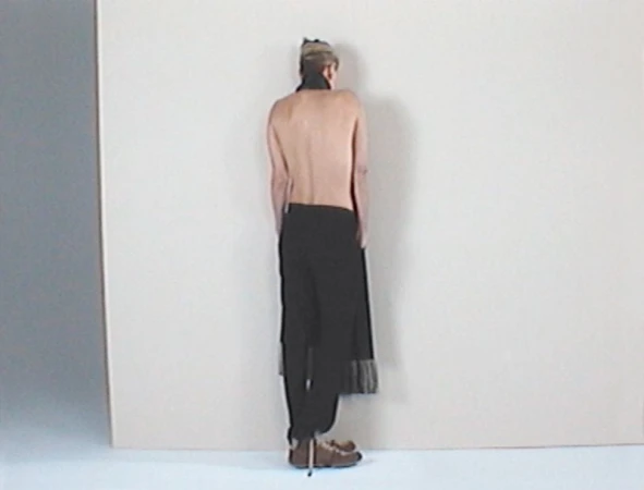 Charlize Theron shown from behind wearing dark trousers against a pale studio background for AnOther Magazine.