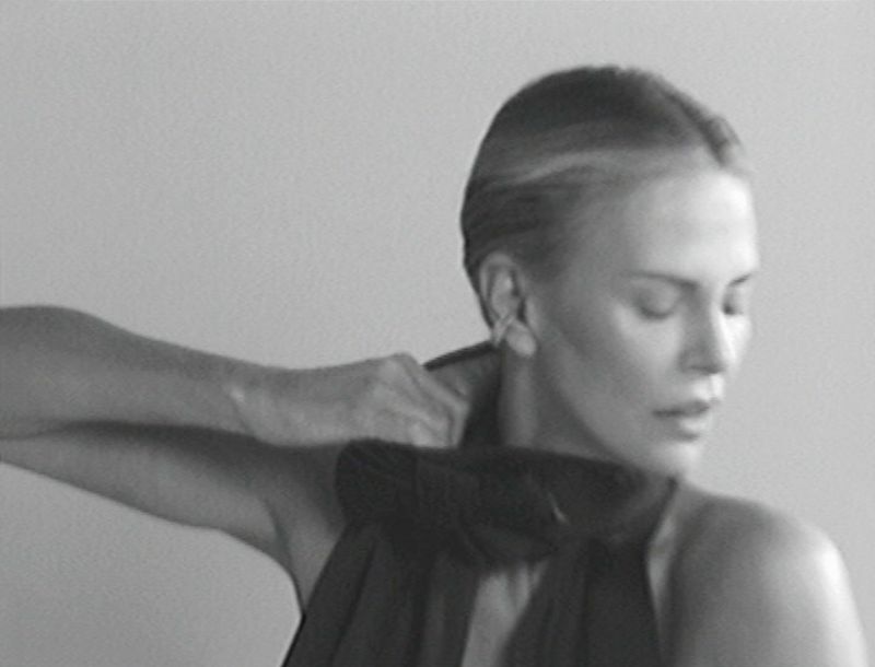 Monochrome portrait of an adult woman adjusting a dark top, close-up shot against a grey background, creating a timeless and classic image.