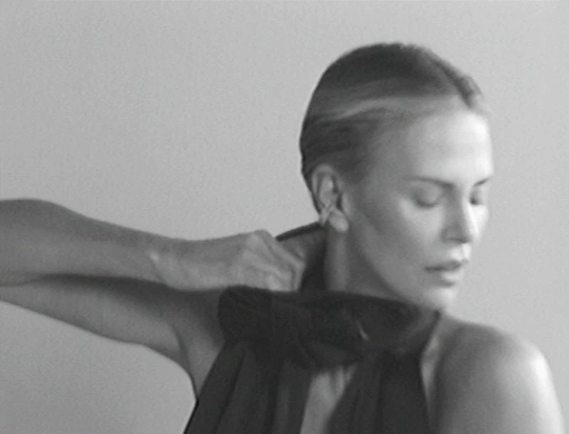 Monochrome portrait of an adult woman adjusting a dark top, close-up shot against a grey background, creating a timeless and classic image.