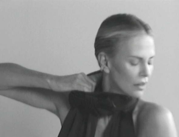 Monochrome portrait of an adult woman adjusting a dark top, close-up shot against a grey background, creating a timeless and classic image.