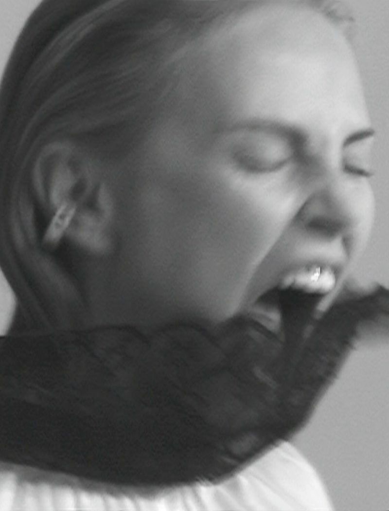 Black and white portrait of a woman with closed eyes with an arm covered in a lace sleeve in her mouth in a studio setting.