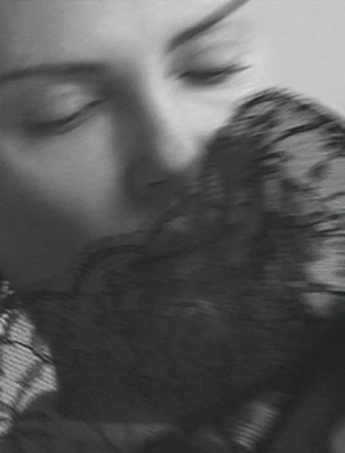Monochrome close-up of a woman with eyes closed, partially veiled by black lace, creating an intimate and sensual black and white image.