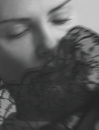 Monochrome close-up of a woman with eyes closed, partially veiled by black lace, creating an intimate and sensual black and white image.