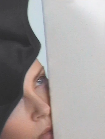 Close-up portrait of actress Charlize Theron looking upward past a pale upright panel and black fabric.