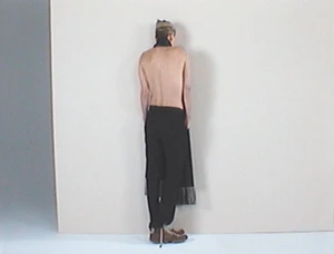 Charlize Theron shown from behind wearing dark trousers against a pale studio background for AnOther Magazine.