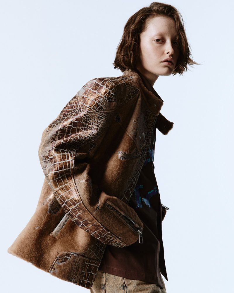 Fashion shot of a female model wearing a brown, crocodile-print jacket against a bright background, showcasing style and texture.