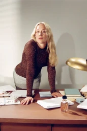 Chloe Sevigny leaning over a desk in an office setting for the Miu Miu fragrance campaign