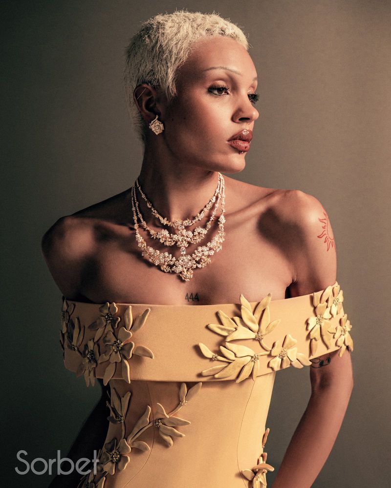 Elegant fashion portrait of a person wearing a yellow off-the-shoulder gown with floral embellishments and a statement pearl necklace.