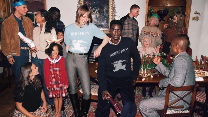 Group portrait of multi-generational family gathering indoors, wearing Burberry sweaters and party hats, seated at dining table with food.