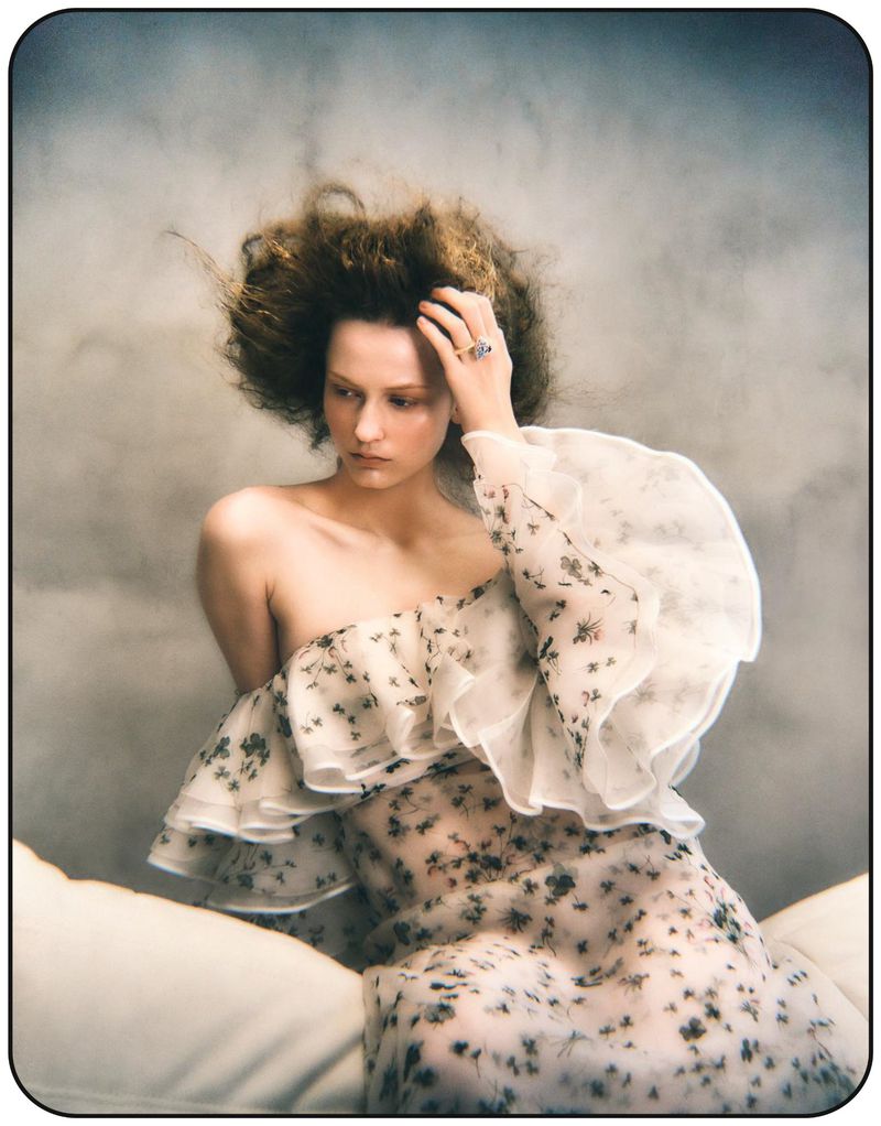 Woman in a floral dress sits in a studio with soft lighting and a diffused background, creating an ethereal and fashionable portrait.