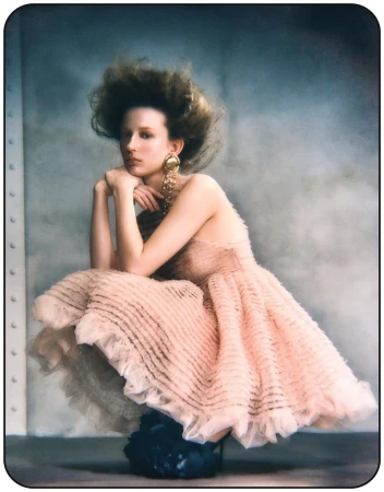 Model Melinda Kiss crouches wearing a ruffled pink dress and statement gold earrings for Harper's Bazaar Germany