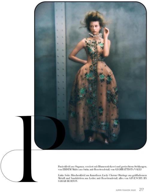 A slender model poses gracefully in a flowing, peach-colored gown with floral accents against a neutral backdrop, embodying high fashion.
