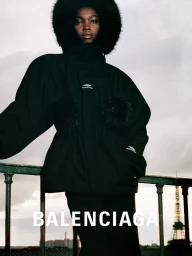 Model in black ski jacket with faux fur hood posing against an outdoor balcony with an Eiffel Tower silhouette