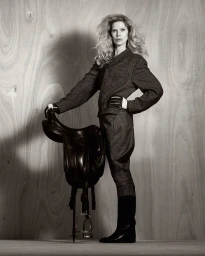 Model Iselin Steiro standing beside a leather saddle in a patterned tweed suit for D Repubblica by Drew Vickers