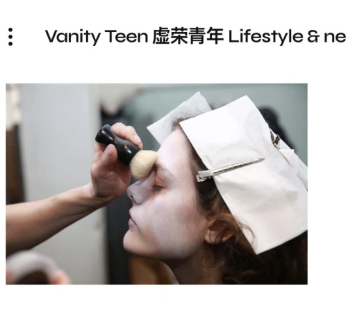 Makeup artist applies powder with a brush to a model's face with tissue and a clip in her hair in an indoor setting.