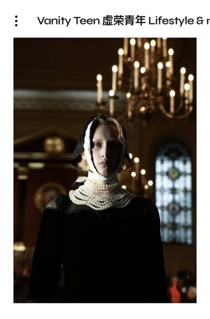 Fashion editorial shot: woman in a black dress and pearl necklace with an ornate chandelier in the background.