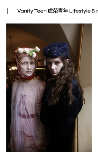 Two models pose in vintage-inspired fashion featuring headpieces with netting and floral accents. The image has an editorial feel.